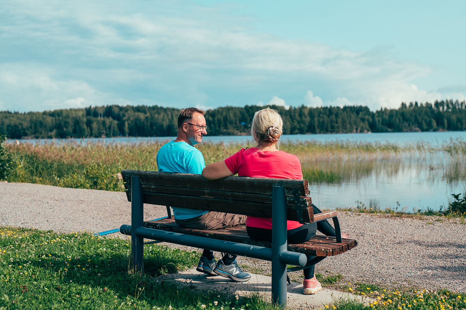 Pariskunta istuu penkillä fiilistellen toisiaan ja järvimaisemaa.