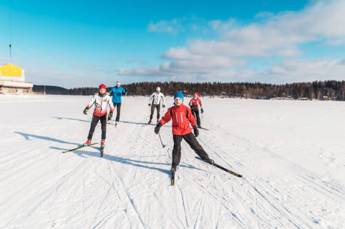 Viiden hengen perhe hiihtämässä Pajulahdessa, jäätyneen kukkasjärven lumella.