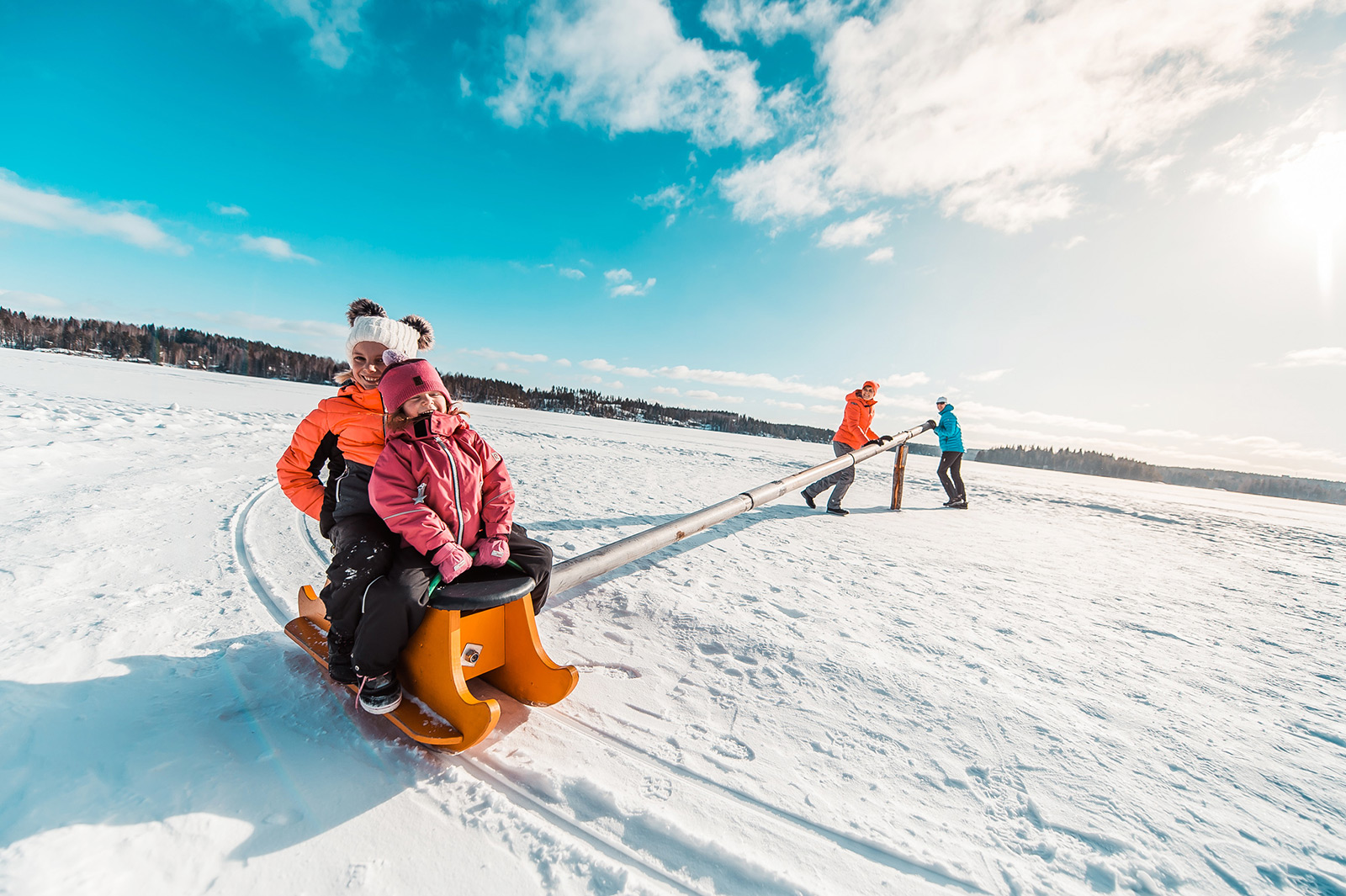 Äiti ja isä pyörittää kahta lastaan napakelkassa Pajulahdessa kukkasjärven jään lumella.