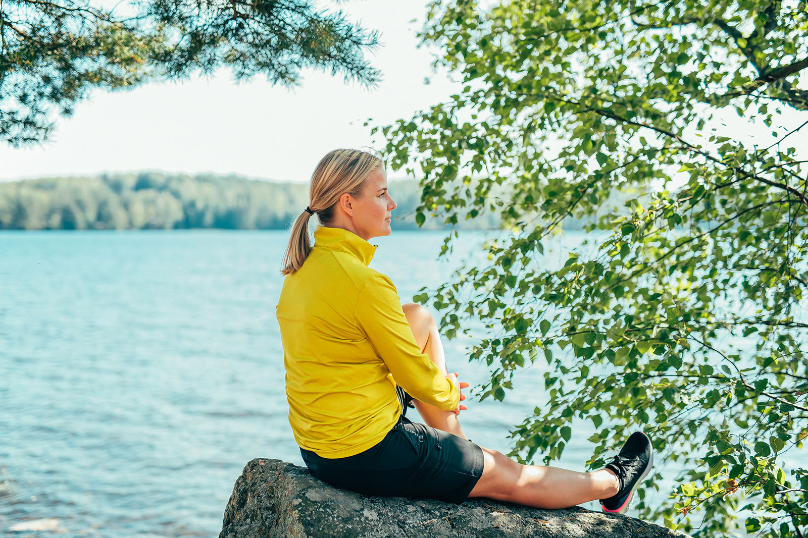 Nainen istumassa rantakivellä, ihastellen Pajulahden järvimaisemaa.