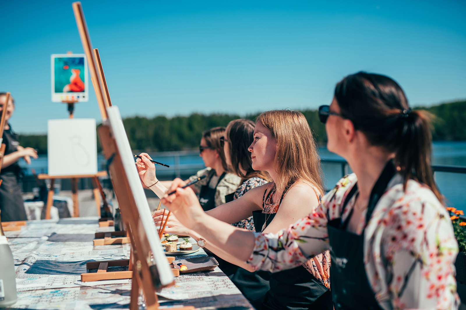 Paint & Partyssa neljän naisen ryhmä maalaavat omia taulujaan rantaterassilla Pajulahdessa.