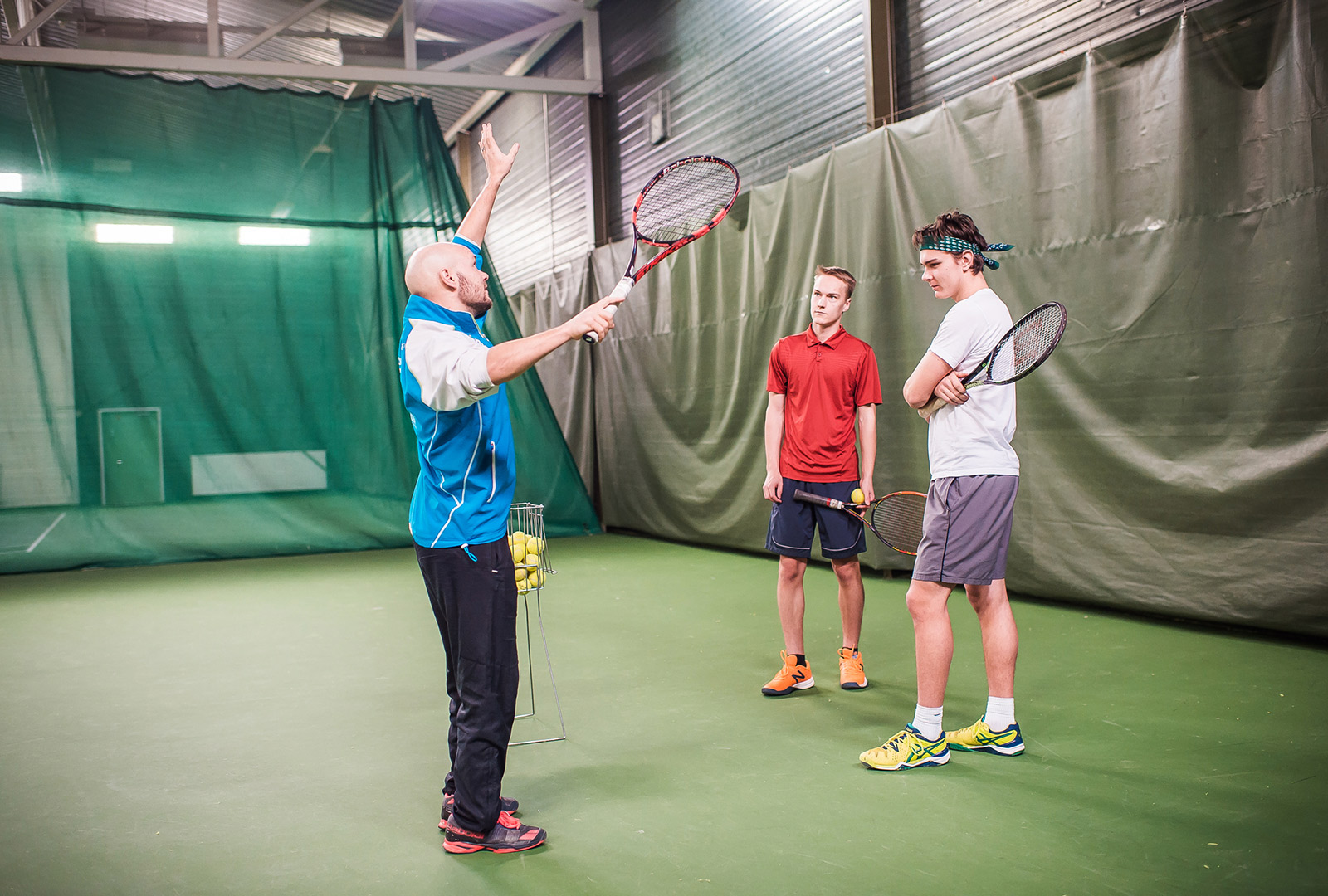 Tennisvalmentaja opastaa miehiä tennismaila kädessä.